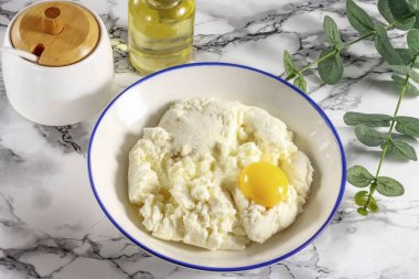 Herhangi bir yağ içeriğinin süzme peynirini derin bir kaba koy, tavuk yumurtasının içine dök ve psyllium, tuz ekle. Her şeyi nazikçe çatalla karıştır..