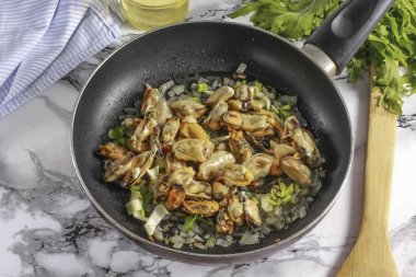 Bir dakika kızart ve yıkanmış midyeleri de ekle. 2-3 dakika daha kızart, zaman zaman her şeyi karıştır..