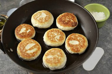 Sonra, bir kaşıkla biraz kaymak kütlesi alın, istenen şekil ve boyutta peynirli kekler yapın, altın kahverengiye kadar en az rafine edilmiş sebze yağında tavada kızartın..