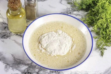 Buğday unu dök ve yavaşça hamurun içine katla. 20 ml dök. sebze yağı ve karıştırma. Glüteni aktifleştirmek için 15 dakika izin al..