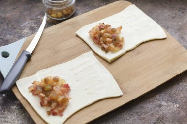 Mangırın buzunu çözün ve yuvarlayın, dikdörtgenlere ayrılın. Hamurun yarısına bir çorba kaşığı elma ve kuru üzüm koy. Hamurun ikinci yarısında yarık aç..