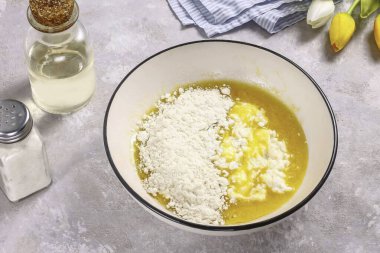 Yağlı içerikli süzme peyniri çırpılmış kütlenin içine koy ve parça parça buğday unu ekle. Kabartma tozunu da karıştır..