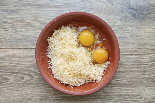 Grate the cheese on a medium grater and set aside a little for the top. Crack the eggs into a bowl of cheese.