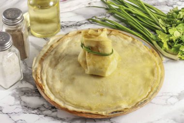 Krepin kenarlarını bir torba yapmak için üst tarafa toplayın. Yırtılmamaya dikkat ederek, onları nazikçe yeşil soğan tüyüyle bağla. Benzer şekilde, kreplerin geri kalanına da başla..