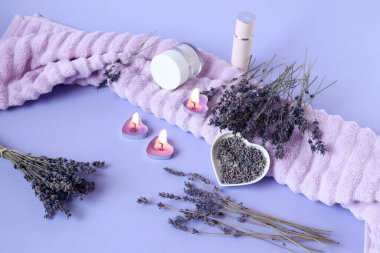 Aromatik bitkiler kullanma kavramı: kuru lavanta dalları arasında vücut bakımı ürünleri ve pastel arka planda banyo havlusunda mum yakma kavramı