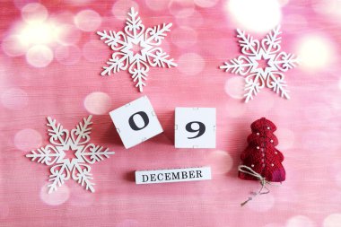 9 Aralık takvimi: 0 ve 9 numaralı küpler, İngilizce ayın adı, dekoratif kar taneleri ve pembe arka planda bir Noel ağacı, bokeh