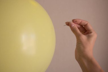 Balonu patlatmak için elinde bir iğne tutuyor.