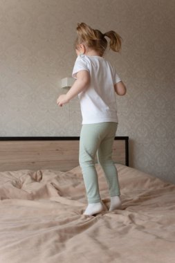 Küçük kız neşeyle yatakta zıplıyor.