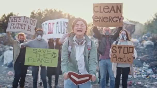 Portret atrakcyjnej młodej aktywistki trzymającej znak stopu. W tle Walka z ludźmi protestującymi przeciwko zanieczyszczeniu śmieciami Pobyt na wysypisku śmieci na obrzeżach miasta. — Wideo stockowe