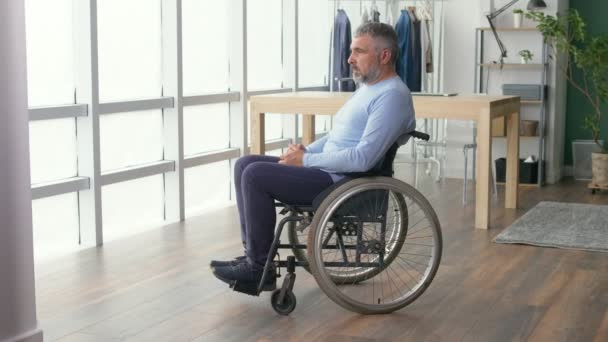 Mężczyzna patrząc przez okno, sfrustrowany Dojrzały Mężczyzna siedzi na wózku inwalidzkim — Wideo stockowe