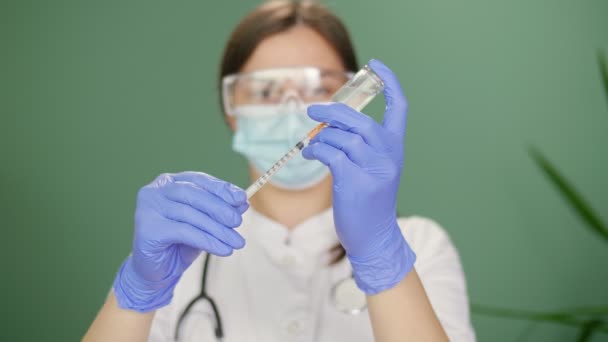 Un médico con máscara médica y guantes azules sostiene una jeringa y una vacuna. — Vídeos de Stock