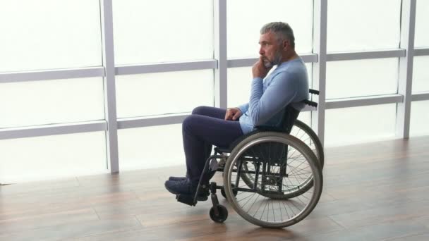 Un homme assis seul dans un fauteuil roulant près de la fenêtre. Solitude, Soins, Retraite — Video