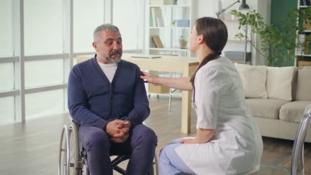 Um homem de meia-idade numa cadeira de rodas a falar com uma enfermeira. Conceito de Apoio à Saúde — Vídeo de Stock