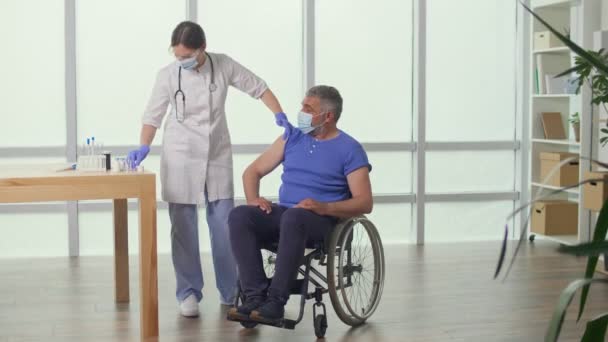 Un homme d'âge moyen en fauteuil roulant qui reçoit le vaccin à la clinique. — Video