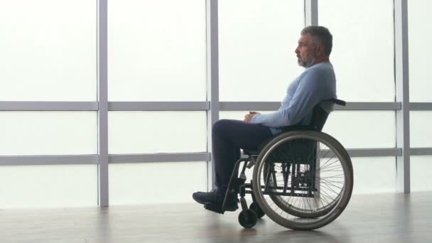 Самотній чоловік середнього віку сидить у інвалідному візку біля вікна . — стокове відео