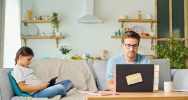 Kendini tecrit sırasında, Baba dizüstü bilgisayarda çalışır ve Kız Kanepede otururken ödevini yapar. Çocuk uzaktan kumandayla tablet kullanmayı öğreniyor. Uzaklık Öğrenme Konsepti