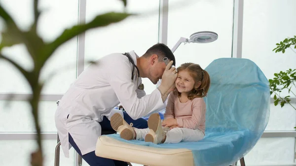 İlgili bir doktor küçük bir kızın kulağını özel bir aletle muayene eder..