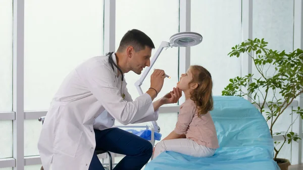 아동 환자가 의사 사무소를 방문하다. 닥터는 청진기를 사용하여 어린이의 폐에 주의를 기울이고, 어린 소녀와 함께 말한다. 진료소에서 자녀를 위로 할 수있다. — 스톡 사진
