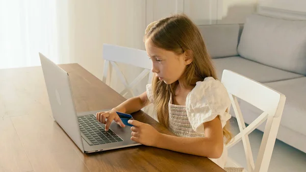 Niño trabajando en su computadora portátil en casa y hacer alguna operación con una tarjeta de crédito. Educación moderna. Protección de datos.Educación financiera de un niño — Foto de Stock