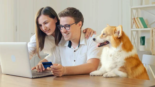 Веселая молодая пара с собакой покупки в Интернете, сидя дома. Взаимные семейные покупки. — стоковое фото