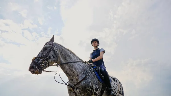 Junge Jockeyspielerin auf einem Pferd im Freien. Sportlerin reitet Pferd auf offener Manege — Stockfoto