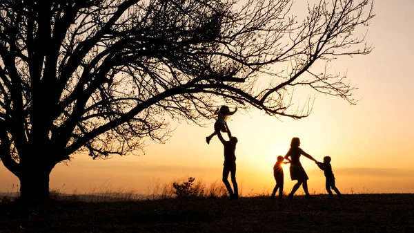 Silhouetten van familie tijd doorbrengen samen in de wei in de buurt van tijdens zonsondergang — Stockfoto