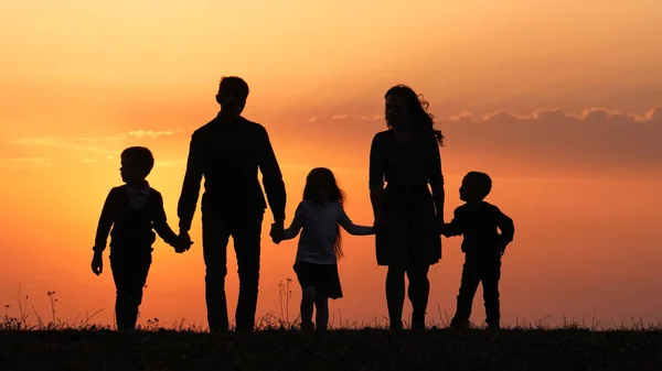 Siluetas de familia feliz sosteniendo las manos en el prado durante el atardecer . —  Fotos de Stock