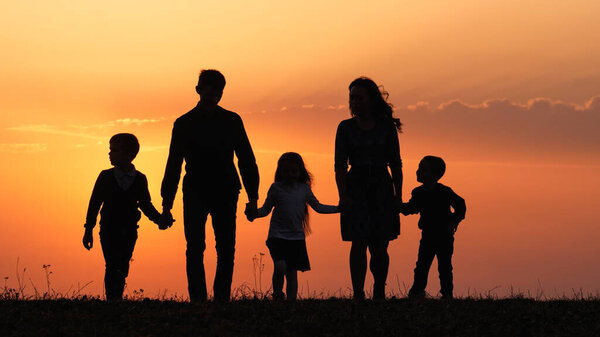 Silhouettes of happy family holding the hands in the meadow during sunset.