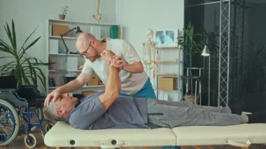 Doktor beyin felçli yaşlı bir adamla fizik tedavi seansı düzenliyor.