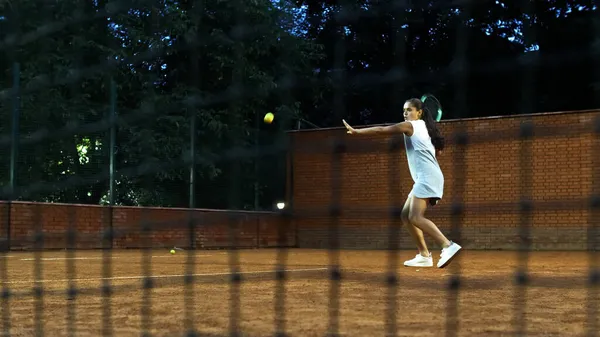 Jugar al tenis por la noche. Chica joven bloqueando la pelota con la raqueta de tenis durante el entrenamiento — Foto de Stock