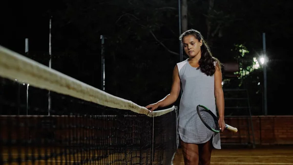 La chica tenista camina por la red de tenis. Jugar al tenis por la noche . — Foto de Stock