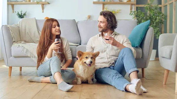 Happy Young Menikah Pasangan Duduk di Lantai Dekat Couch dan Clinking Gelas Dengan Anggur Stok Gambar