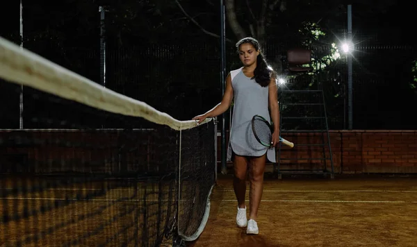 La chica tenista camina por la red de tenis. Jugar al tenis por la noche . —  Fotos de Stock