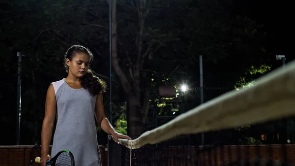 La chica tenista camina por la red de tenis. Jugar al tenis por la noche . — Foto de Stock