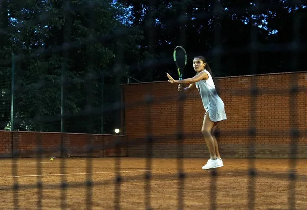 Jugar al tenis por la noche. Chica joven bloqueando la pelota con la raqueta de tenis durante el entrenamiento — Foto de Stock