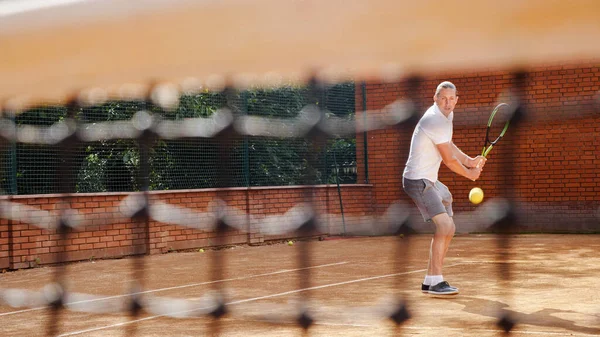 Joven atractivo hombre jugando tenis en naranja arcilla pista de tenis — Foto de Stock