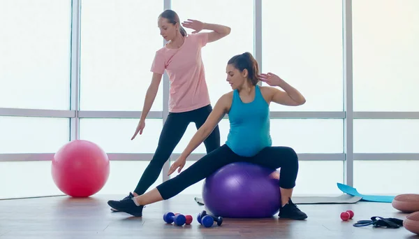 Zwangere vrouw doet oefeningen voor zwangere vrouwen met een personal trainer Rechtenvrije Stockafbeeldingen