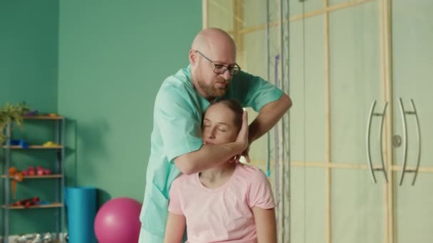 Fysioterapeut hjälper flicka att göra övningar för att lindra smärta i Rehab Clinic. — Stockvideo
