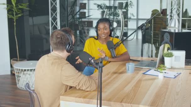 En man Presenter kommunicerar med en gäst, en afroamerikan, i en studio. — Stockvideo