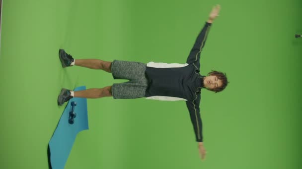 縦の映像 ハンサムなスポーティメキシコ人男性が呼吸法を行う緑の画面の背景に手を上下に上げる マットとダンベルは彼の近くに横たわっています 国内物理的ジャーク — ストック動画