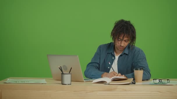若い多文化学生のフリーランスノートパソコンを探して オンライン宿題をして 緑の画面の背景にある紙のノートブックと教科書にタスクを書き換えます ビューを閉じる — ストック動画