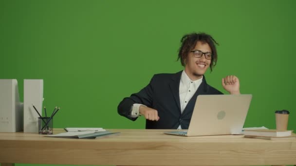 若い多文化ビジネスマンフリーランサーノートパソコンの作業台に座り カメラと笑顔を眺めながら 椅子の上でエネルギーダンスを行ったり来たり 緑の画面で手を叩く背景 — ストック動画