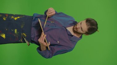 Dikey Görünüm, Dikey Görünüm. Cebinde Fırçayla Genç Sakallı Adam Palette Akrilik Boyaları Karıştırıyor ve Kameraya Bakıyor ve Yeşil Ekranda Gülümsüyor, Chroma Anahtarı. Yaratıcılık ve Sanat Konsepti