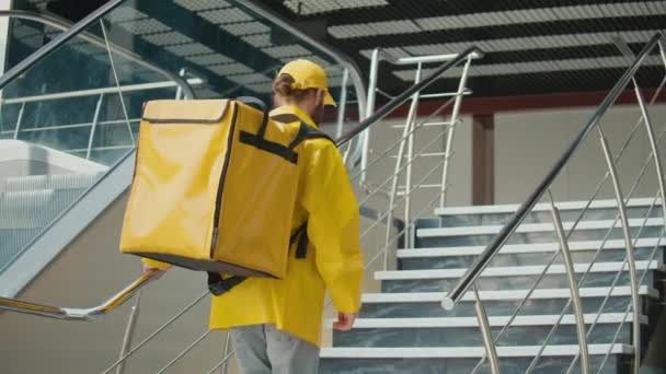 Доставщик Продуктов Питания Жёлтой Униформе Термальным Рюкзаком Поднимающимся Лестнице Современном — стоковое видео
