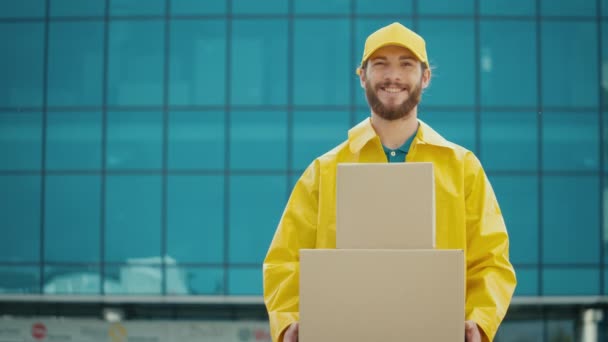 黄色の制服でハンサムな配達人の肖像は 段ボール箱と笑顔を保持しています 宅配便物流センターで働く オンライン注文を提供 素晴らしい配達サービス — ストック動画
