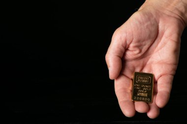 Siyah arka planda küçük altın külçeler tutan bir el.