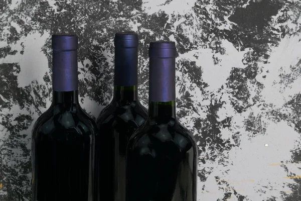 Top of three red wine bottles with purple caps on gray and black background .