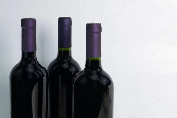 Top of three red wine bottles with purple caps on white background