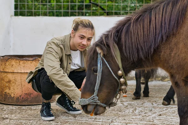 Uzun sarı saçlı genç bir adam midilliyi besliyor.
