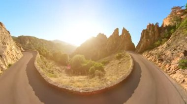 Aerial view of Les Calanques of Piana, a natural park of Corsica on the Mediterranean and UNESCO heritage. Red car on the road D81 route of the Piana Badlands at twilight.